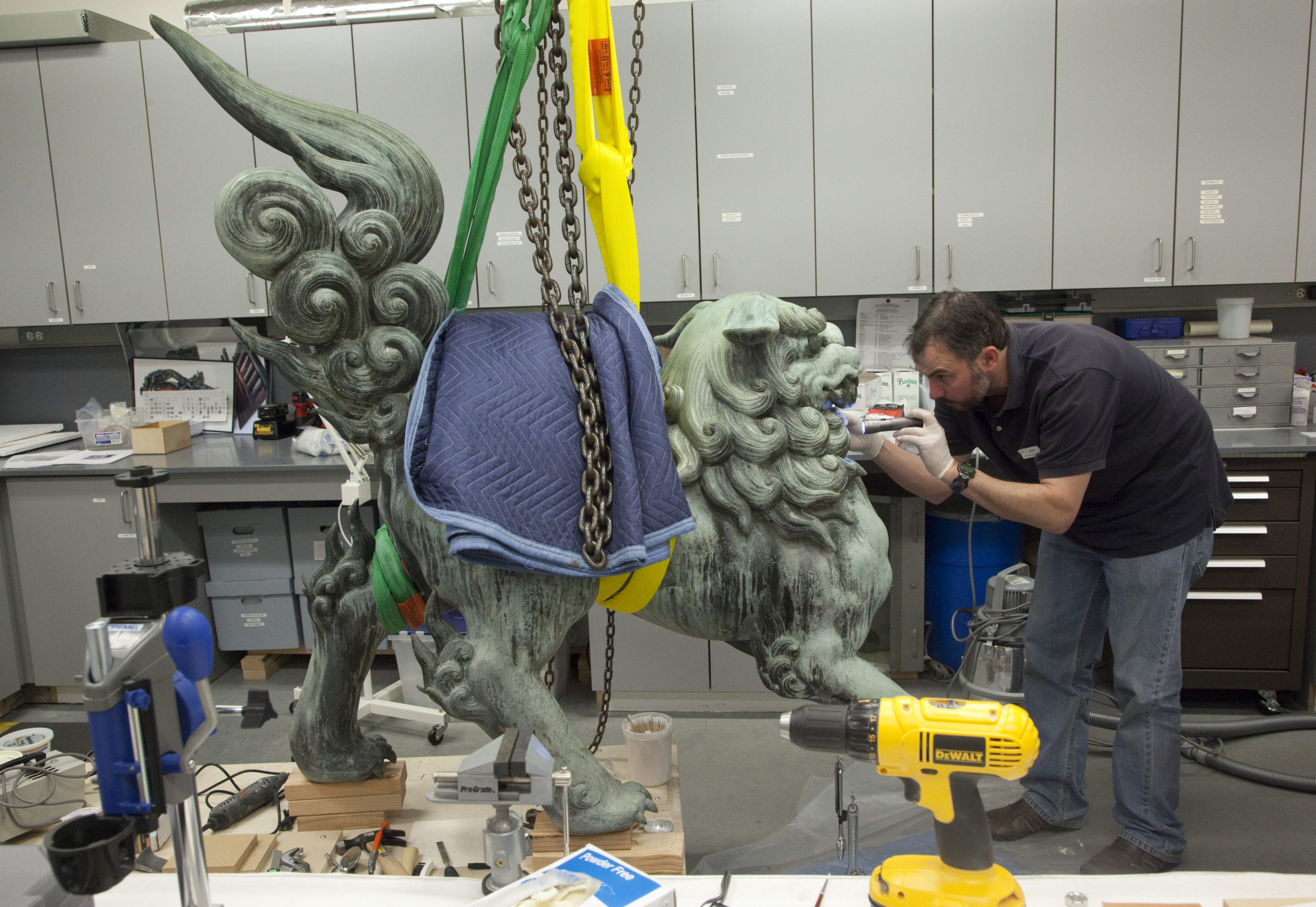 A conservator works on a bronze lion statue.