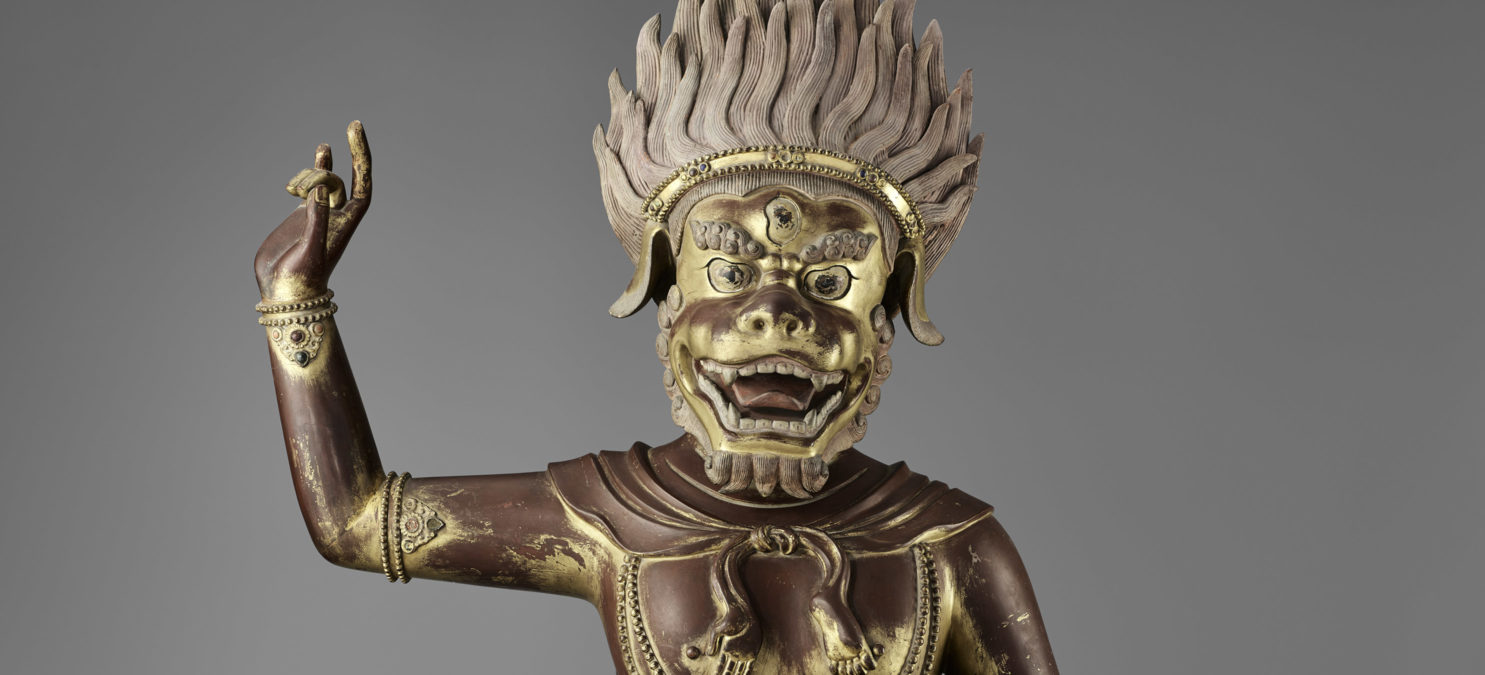 A figure of a Buddhist deity standing on its left leg and its right arm extended upward.