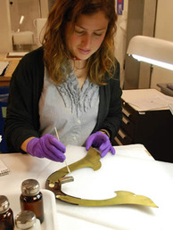 A conservator works on a helmet crest.